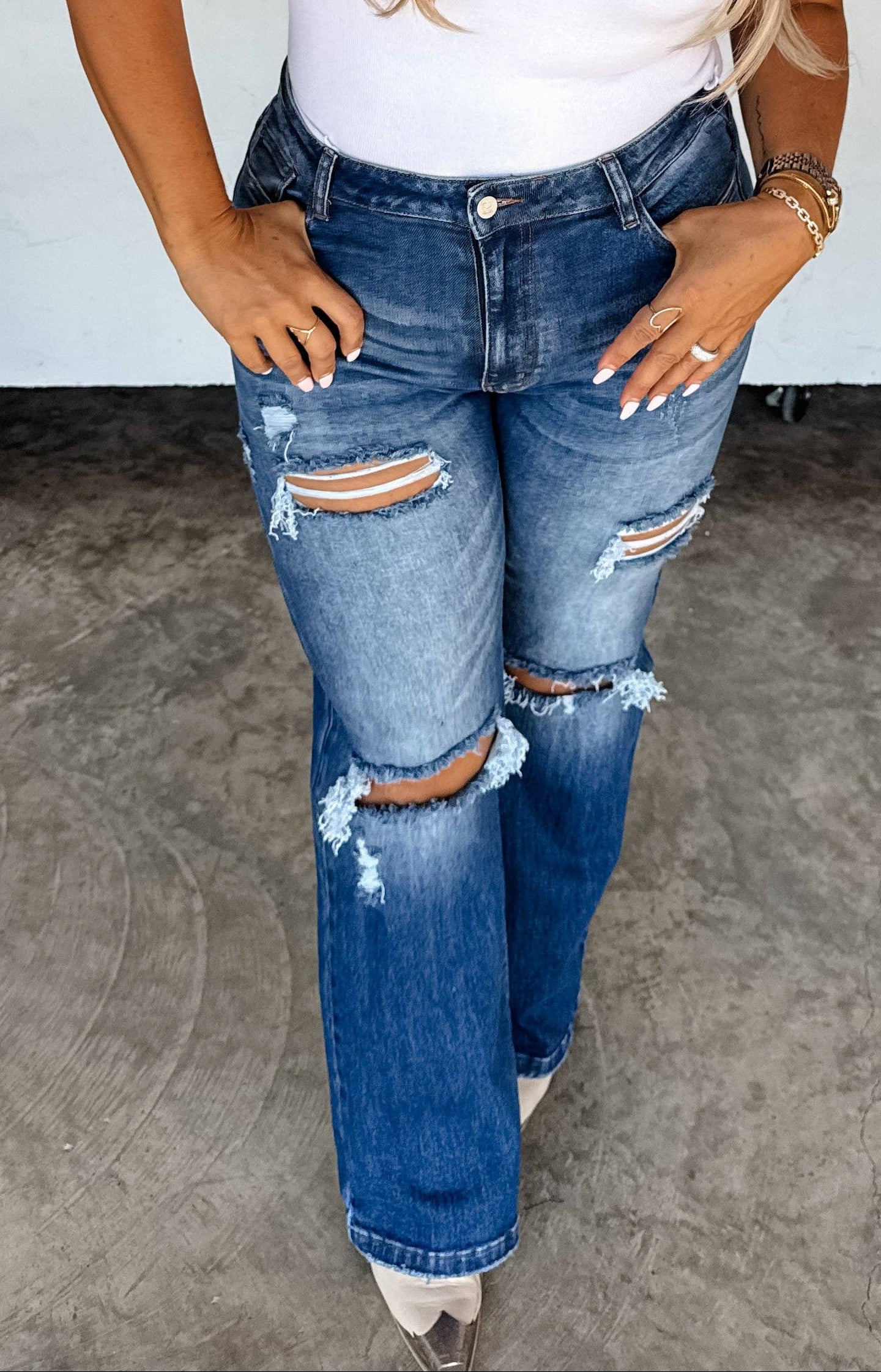 Woman wearing a white sleeveless top, blue jeans, and a brown cap with a horse shoe logo.